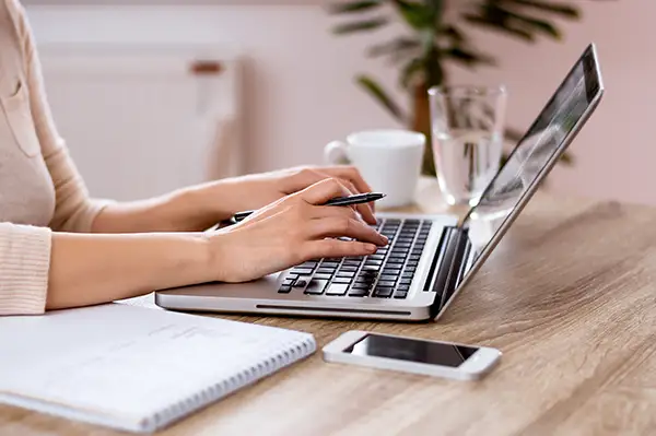 A woman writing a dental blog article on her laptop with a pen and notepad besides her. A woman writing a dental blog article on her laptop with a pen and notepad besides her.