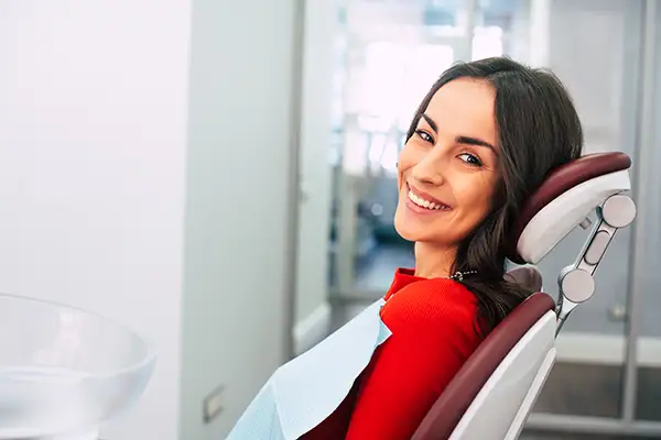 A woman smiling brightly in the dentist chair with a bib on, waiting for her first dental appointment. A woman smiling brightly in the dentist chair with a bib on, waiting for her first dental appointment.